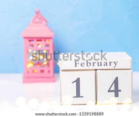 Calendar, pink candleholder with fairy lights on white fur background against blue wall. Selective focus. Place for text.