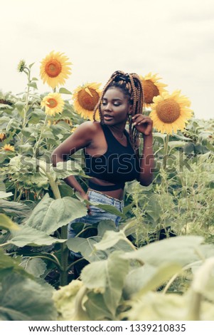 Outdoor portrait of beautiful happy mixed race African American girl teenager female young woman in a field of yellow flowers at sunset golden evening sunshine