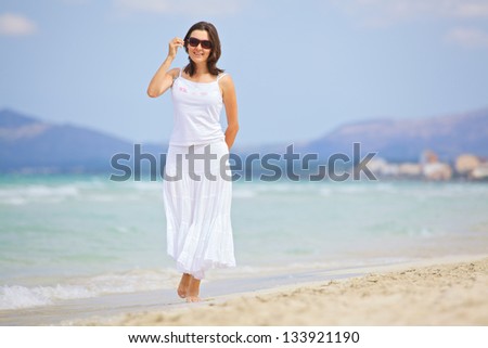 Beautiful young woman walking on the beach enjoying the sun