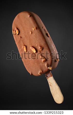 Brown chocolate ice cream popsicle with peanuts on black background