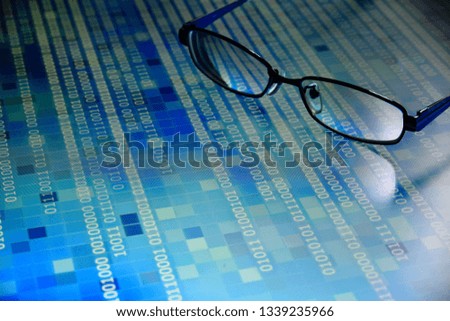 big data analysis. blue binary code on led panel with black background and eyeglasses placed over the information panel. hacker and source code analysis.