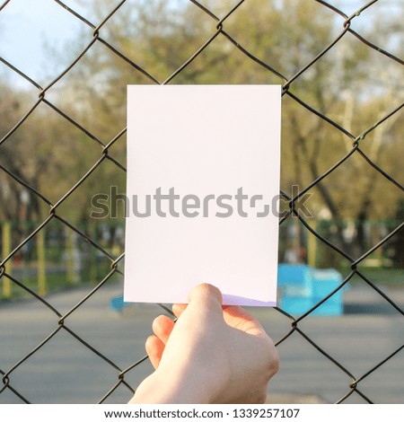 Mock up card, post card or advertising leaflet of standard A5 size on against the background of a metal fence with a grid
