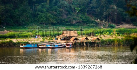 Beautiful traditional huts with green fields in the background and wooden boats anchored on the Mekong River. Luang Prabang is the ancient capital of Luang Prabang Province in northern Laos.