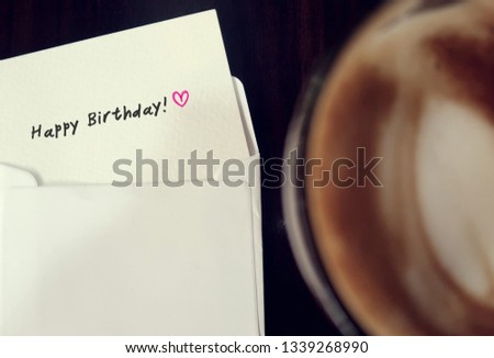 a tiny card in envelope with text message HAPPY BIRTHDAY, with a blurred cup of coffee at  the right side