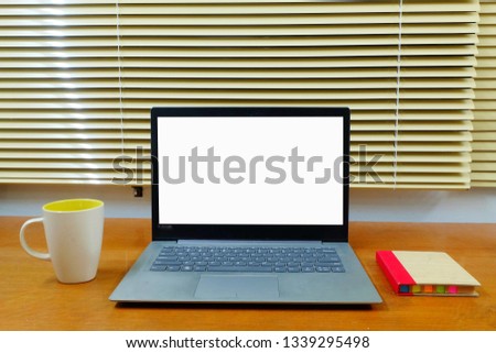 A picture of a laptop with white screen or chroma key on a desk. Insight a cup of hot chocolate and memo pad. It can be used for graphic work or design.