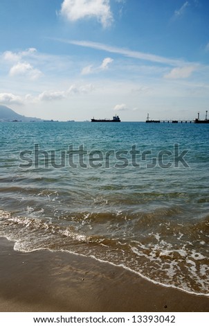 Tranquil wave surf on sand beach and cloudy blue sky, pier with shipping in the background