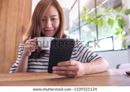 Closeup image of a woman holding , using and looking at smart phone while drinking coffee 