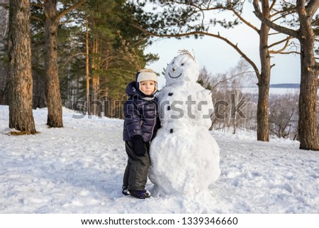 Little boy in red winter clothes having fun with snowman. Active outdoors leisure with children in winter. Kid with warm hat, hand gloves and scarf
