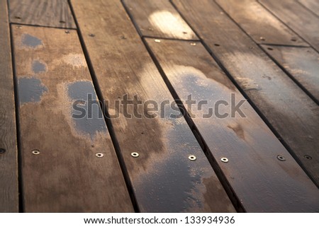 Wooden deck floor of a boardwalk, water sprayed by ricochets splashed off of waves breaking against the boardwalk's wall.