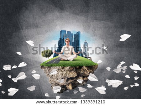 Man in white clothing keeping eyes closed and looking concentrated while meditating on island in the air among flying paper planes with gray dark wall on background. 3D rendering.