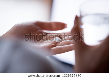 Close up woman holding pill in hand with water. Female going to take tablet from headache, painkiller, medication drinking clear water from glass. Healthcare, medicine, treatment, therapy concept Royalty-Free Stock Photo #1339397660