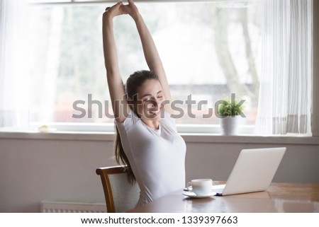 Happy relaxing woman stretching in front of computer at home. Smiling female reach out, put hands up sitting at laptop with eyes closed. People at work, remote work, studying, working online concept
