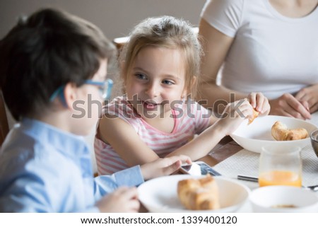 Smiling little girl talking with brother at breakfast at home. Two children interacting eating morning meals, having fun. Boy playing smartphone at dining table. Family lifestyle, gadget addiction