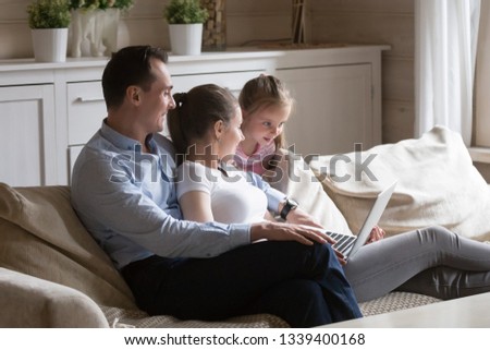 Family relaxing on sofa at home watching movie on computer. Happy people spending time together at home. Mother, father and daughter have leisure time on couch with laptop. Technology, gadgets concept