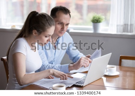Millennial couple studying contract for new house before signing. Husband and wife checking documents for buying property. Real estate purchase, homeowner, loan, credit, mortgage, rent, tenant concept Royalty-Free Stock Photo #1339400174