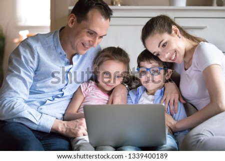 Happy family with kids watching funny video on computer screen. Mother, father, daughter and son smiling seeing good movie or cartoon on sofa at home. Leisure time, weekend evening at home concept
