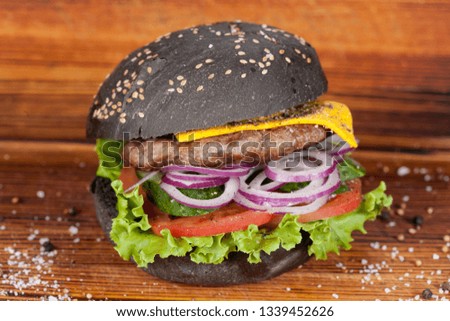 
Fast food, appetizing black burger, beautifully laid out on a wooden background, for culinary design