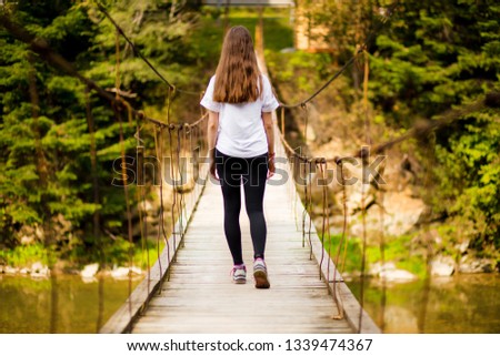 Tourist woman walk by long wooden suspension bridge above river