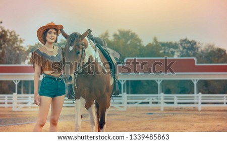 Active Asia cowgirl in hat walking with horse. Farmer girl in countryside ranch. Beautiful woman training and taking care of her horse with love and caring.