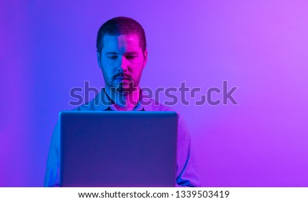 Serious businessman concentrating on his work as he types on a laptop computer in bright vibrant purple studio lighting with copy space
