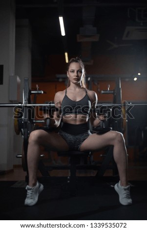 Training pause. Sporty woman in sportswear resting on bench holding dumbbells in her hands in gym