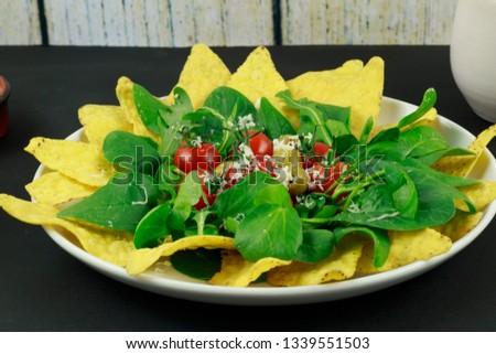 An inviting salad of corn chips, green salad leaves, red cherry tomatoes and green olives.  A sprinkling of Parmesan cheese completes the picture.