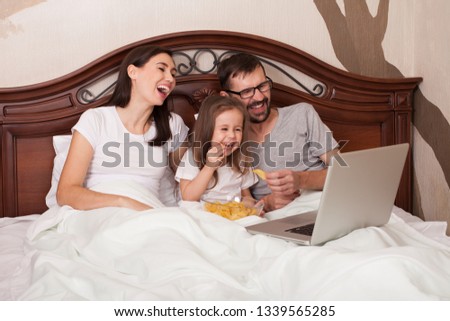 Happy family watching movie in bed and eating chips.