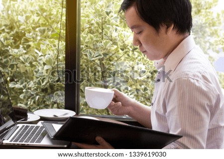 The working man is signing his document with intention, with a cup of coffee and cake in the cafe.Business and technology concept.