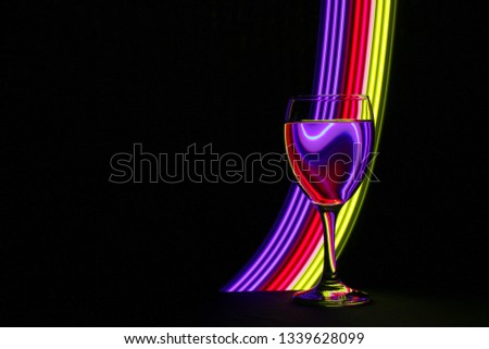 Wine glass isolated against a black background with multicolored neon light painting behind