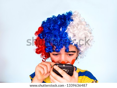 Portrait of funny clown kid holding smartphone and typing text. Pantomimic concept. expression. emotions. April Fool's Day, April 1. Isolated on gray