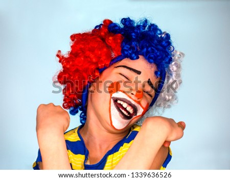 Funny child clown wig enjoying a good joke having a hearty laugh with mouth open and eyes closed as he deviates from the camera.
