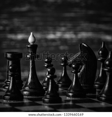 Chess pieces on a wooden chessboard against a dark background. Black and white photography