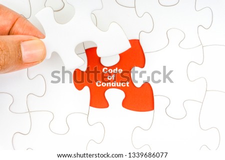 Hand holding piece of jigsaw puzzle with word CODE OF CONDUCT. Selective focus