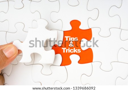 Hand holding piece of jigsaw puzzle with word TIPS & TRICKS. Selective focus