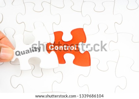 Hand holding piece of jigsaw puzzle with word QUALITY CONTROL. Selective focus