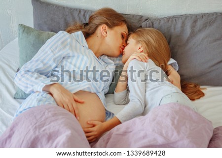 Pregnant mom with her daughter lying in bed and hugging / copy space

