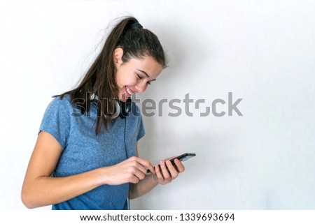 young teenager girl with headphones around her neck fingers typing in a smartphone smiling broadly, wallpaper background