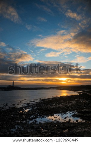 January sunrise over the Northumberland coast in North East England with St Mary's Island on the horizon and a beautifully coloured sky reflected in the waters of the North Sea.