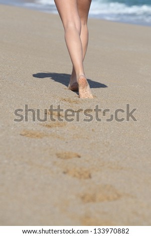 Back view of a woman legs walking on the beach and her traces with the sea in the background
