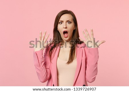 Portrait of shocked young woman wearing jacket keeping mouth open and spreading hands isolated on pastel pink wall background in studio. People sincere emotions, lifestyle concept. Mock up copy space