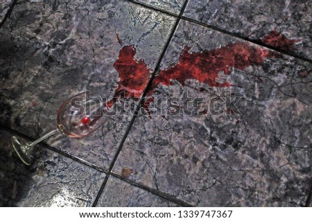 Dramatic glass of red wine spilled on a black and grey floor from an up angle. Ceramic