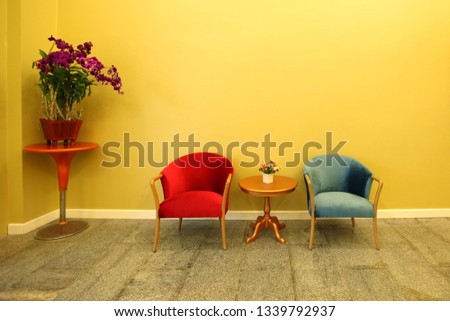 red and green sofa chair on the floor in front of yellow background the side has a red table which has a basket of orchids all on the mable floor
