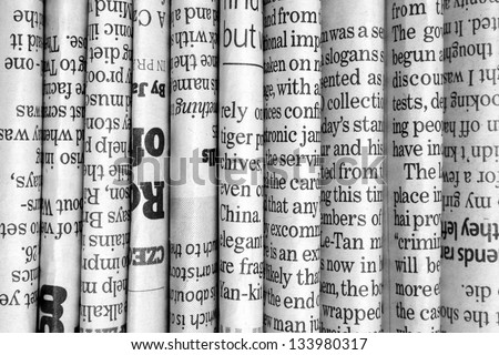 A black and white background of English language newspapers stacked and folded in a vertical position and viewed in close up