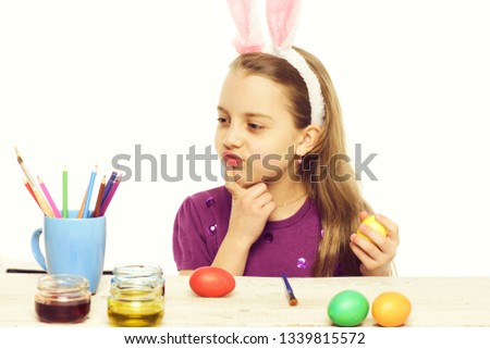 small baby girl or cute child with happy face wearing rabbit pink ears with purple blouse and painting colorful easter eggs isolated on white background
