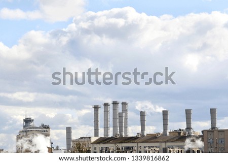 View of the pipes of the plant from which there is white smoke against the sky.