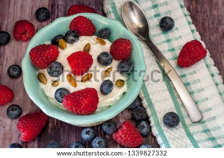 Greek yogurt in a bowl with raspberries, blueberries roasted almonds and pumpkin seeds.