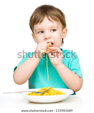 Little boy is eating spaghetti using both hands, isolated over white