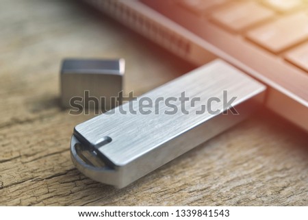Close up of metal USB flash drive connected to laptop on wood desk