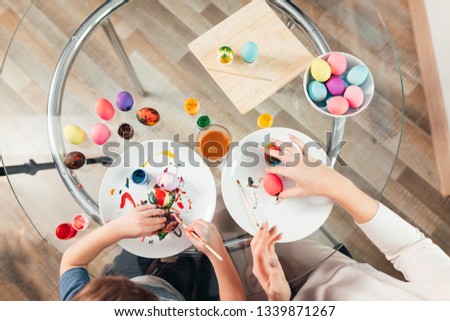 Easter, family, holiday and child concept - top view of little child and mother painting colored eggs on wooden background