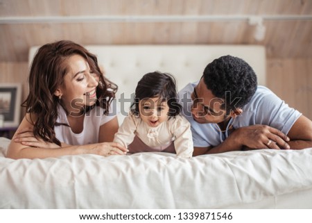 young man anw woman are laughing at their baby crawling daughter, close up photo,tender feeling among members of family